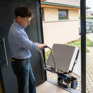 Elektrohersteller Marc Leyre aan het werk bij een klant aan huis. Met een speciale lift werkt hij vakkundig een zware wasmachine over de dorpel zonder die te beschadigen.