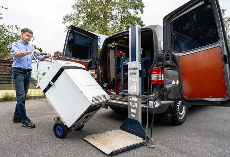 Marc Leyre van Dokter Elektro verplaatst een huishoudtoestel met een steekwagen naar zijn professioneel uitgeruste bestelwagen.