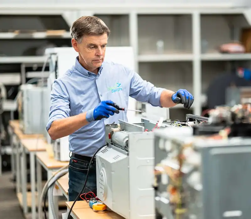 Elektrohersteller Marc Leyre is bezig met het herstellen van huishoudtoestellen in zijn herstelcentrum. Hij werkt aan het herstellen van een wasmachine, een inbouwoven en een vaatwasser.